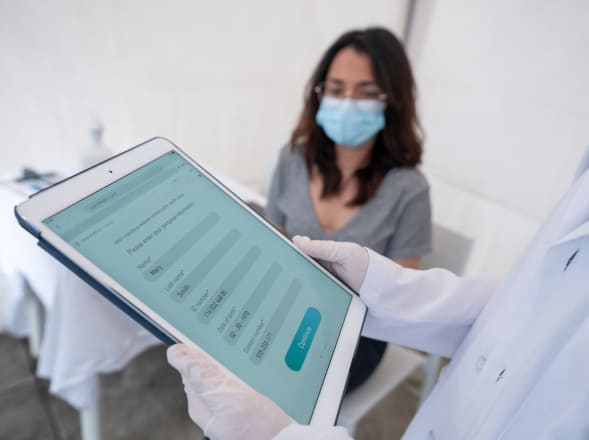Masked patient reviewing medical results on a tablet with a doctor